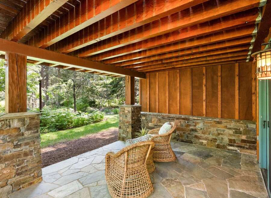 Enjoy the serene outdoors from this charming covered patio, featuring a rustic stone base and a warm wooden ceiling.