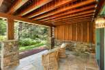 Enjoy the serene outdoors from this charming covered patio, featuring a rustic stone base and a warm wooden ceiling.