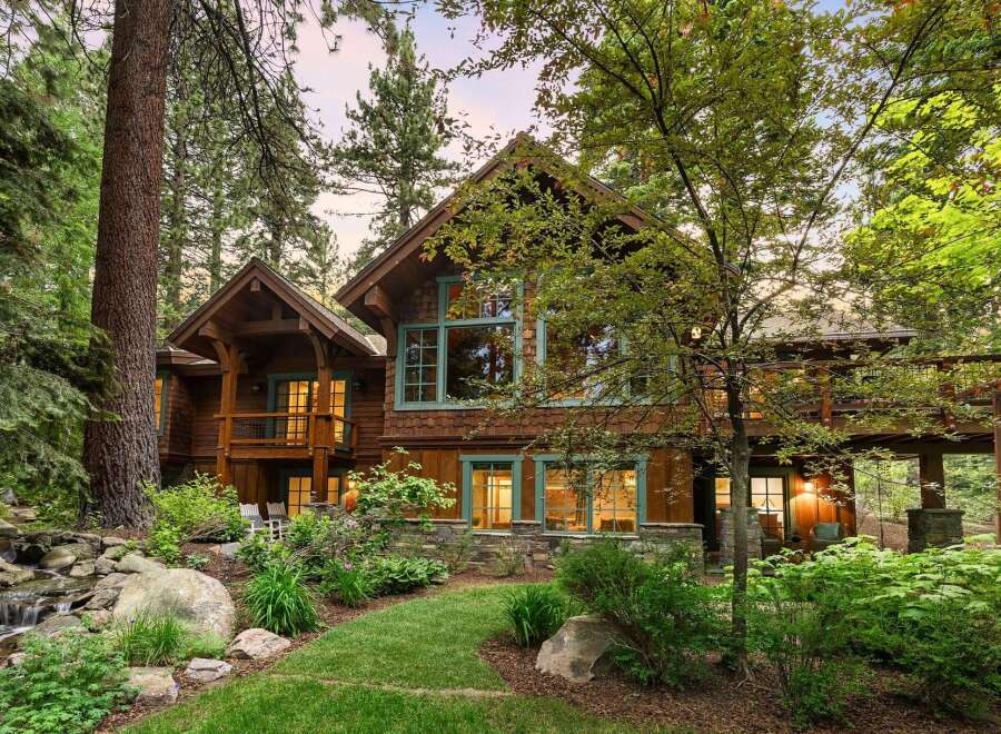 Nestled amidst towering trees, this stunning wooden lodge offers a serene retreat with a charming water feature and lush landscaping.