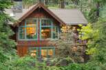 Nestled amidst lush greenery, this charming wooden home features rustic cedar shake siding and striking teal-trimmed windows that add a pop of color.