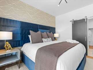Experience luxury in this master bedroom featuring a striking blue velvet headboard and a unique abstract wallpaper accent.