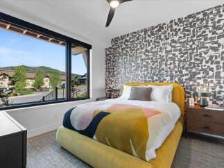 Experience modern comfort in this stylish bedroom featuring a vibrant yellow bed and a striking abstract wallpaper.