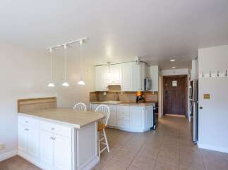 This charming kitchen features white cabinetry, a tiled backsplash, and a spacious island with a tiled countertop, perfect for casual dining or meal prep.