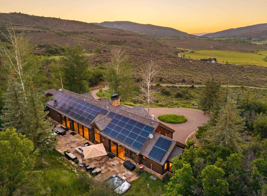 Experience luxury mountain living in this stunning estate, featuring a modern home with expansive solar panels and a spacious stone patio.