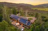 Experience luxury mountain living in this stunning estate, featuring a modern home with expansive solar panels and a spacious stone patio.