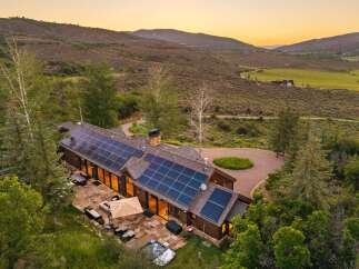 Experience luxury mountain living in this stunning estate, featuring a modern home with expansive solar panels and a spacious stone patio.