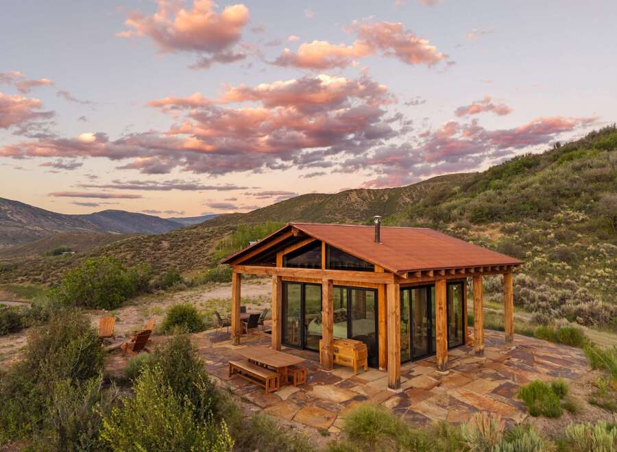 Experience breathtaking mountain views from this modern cabin retreat, featuring expansive glass walls and a rustic wooden exterior.