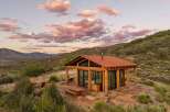 Experience breathtaking mountain views from this modern cabin retreat, featuring expansive glass walls and a rustic wooden exterior.