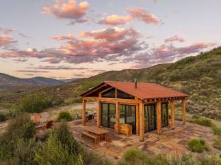 Experience breathtaking mountain views from this modern cabin retreat, featuring expansive glass walls and a rustic wooden exterior.