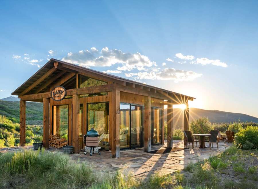 Experience breathtaking sunset views from this modern cabin, featuring expansive glass walls and a covered porch perfect for outdoor living.