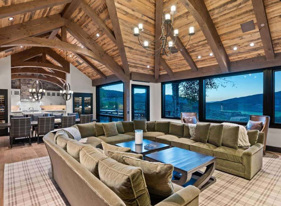 Experience luxury mountain living in this stunning home featuring a grand living room with a massive sectional sofa and a rustic vaulted ceiling with exposed wooden beams.