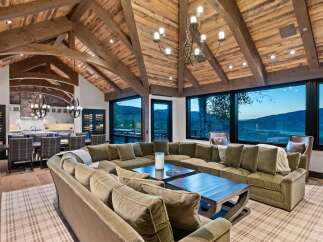 Experience luxury mountain living in this stunning home featuring a grand living room with a massive sectional sofa and a rustic vaulted ceiling with exposed wooden beams.