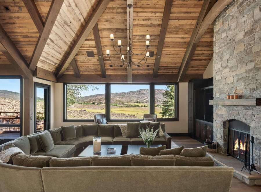 Experience luxurious mountain living in this stunning great room, featuring a massive stone fireplace and a vaulted wood-beamed ceiling.