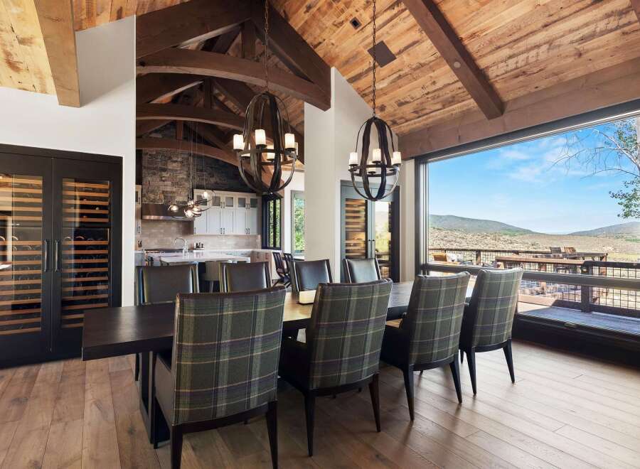 Experience luxury mountain living in this stunning dining room, featuring a grand wooden beamed ceiling and a breathtaking panoramic view of the surrounding landscape.