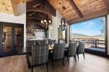 Experience luxury mountain living in this stunning dining room, featuring a grand wooden beamed ceiling and a breathtaking panoramic view of the surrounding landscape.