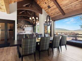 Experience luxury mountain living in this stunning dining room, featuring a grand wooden beamed ceiling and a breathtaking panoramic view of the surrounding landscape.