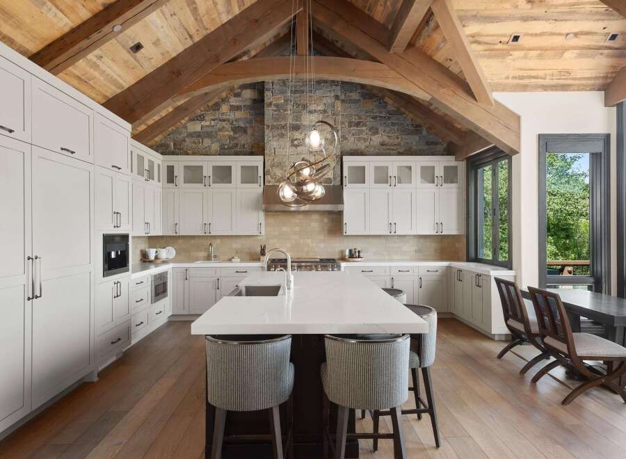 Experience luxury mountain living in this stunning gourmet kitchen, featuring custom white cabinetry, a large island with a waterfall countertop, and a professional-grade range.