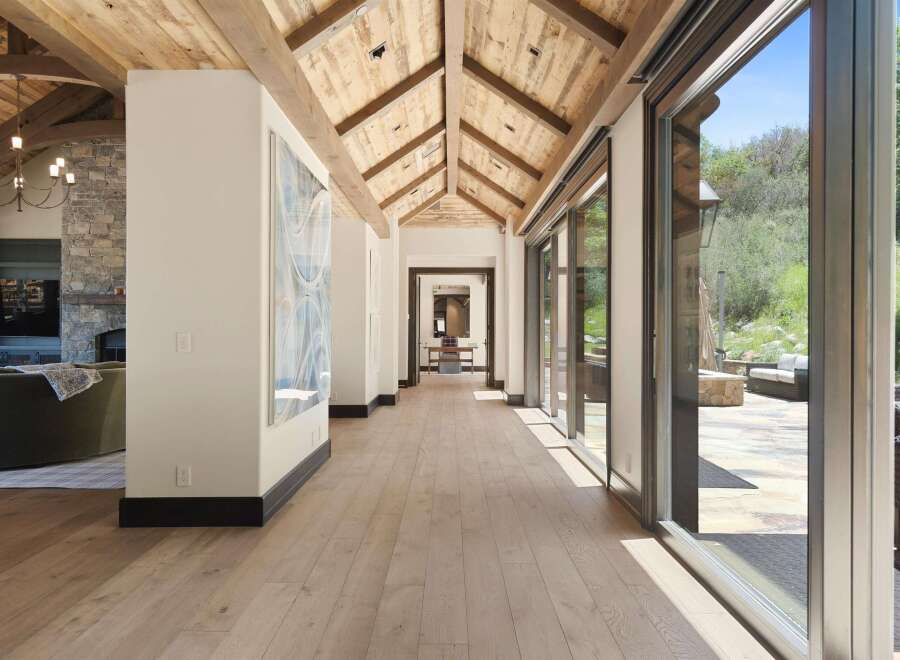 Experience luxury living in this stunning home featuring a grand hallway with a vaulted wood-beamed ceiling and expansive glass doors that open to a serene outdoor patio.