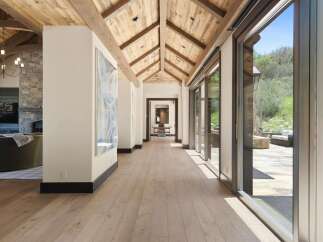 Experience luxury living in this stunning home featuring a grand hallway with a vaulted wood-beamed ceiling and expansive glass doors that open to a serene outdoor patio.