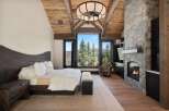 Experience luxury mountain living in this stunning bedroom featuring a grand stone fireplace and expansive windows with breathtaking views.