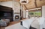 Experience luxury mountain living in this stunning bedroom featuring a grand stone fireplace and a vaulted wood-beam ceiling.