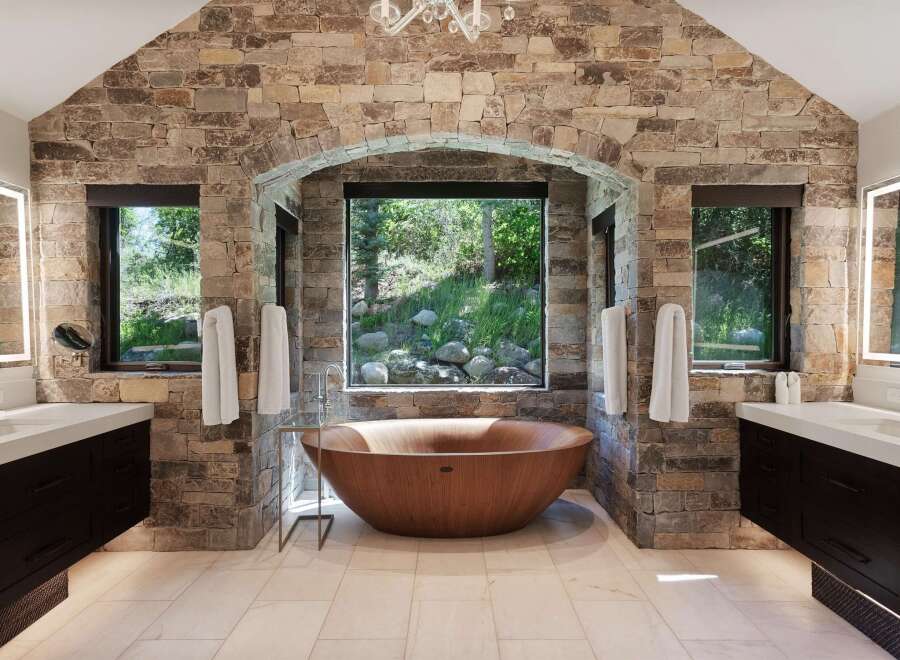 Experience luxury in this stunning bathroom featuring a natural stone accent wall and a unique wooden soaking tub.