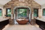 Experience luxury in this stunning bathroom featuring a natural stone accent wall and a unique wooden soaking tub.
