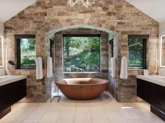 Experience luxury in this stunning bathroom featuring a natural stone accent wall and a unique wooden soaking tub.