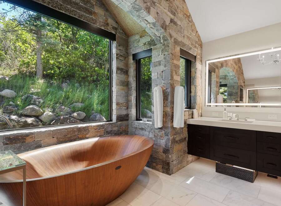 Experience ultimate relaxation in this luxurious bathroom, featuring a stunning wooden soaking tub with breathtaking views of the surrounding nature.