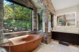 Experience ultimate relaxation in this luxurious bathroom, featuring a stunning wooden soaking tub with breathtaking views of the surrounding nature.
