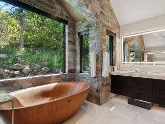 Experience ultimate relaxation in this luxurious bathroom, featuring a stunning wooden soaking tub with breathtaking views of the surrounding nature.