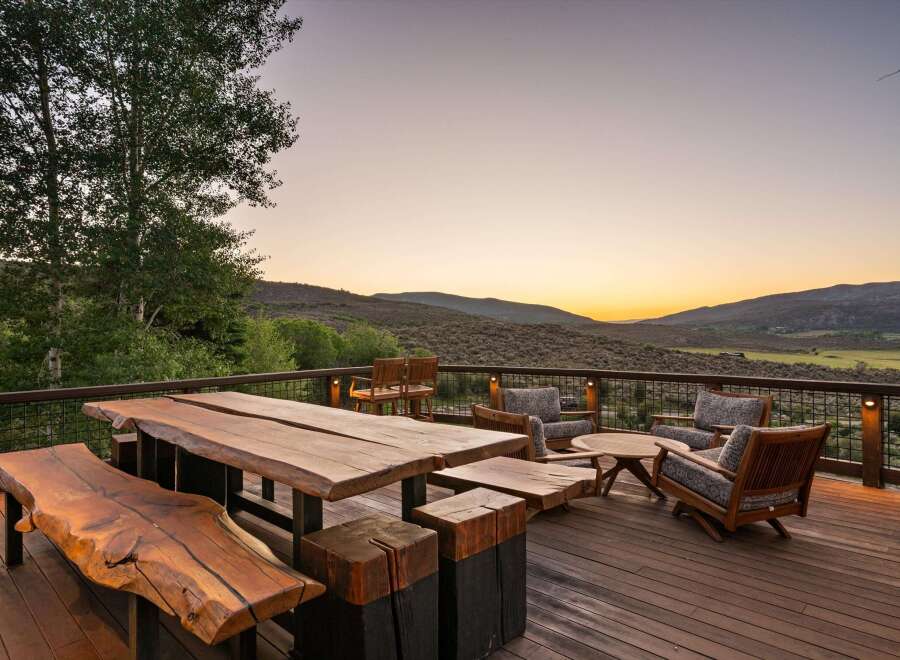 Experience breathtaking sunset views from this expansive deck, featuring rustic live-edge dining furniture and comfortable seating areas.