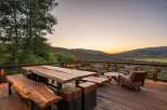 Experience breathtaking sunset views from this expansive deck, featuring rustic live-edge dining furniture and comfortable seating areas.