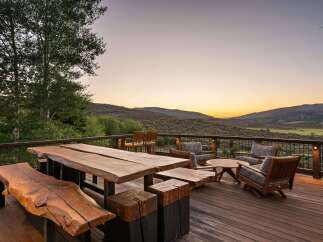 Experience breathtaking sunset views from this expansive deck, featuring rustic live-edge dining furniture and comfortable seating areas.