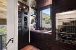 This stunning home bar features a dark wood cabinet with glass doors displaying elegant glassware, complemented by a brick accent wall and a large window offering scenic views.