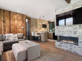 Experience modern mountain living in this stunning open-concept living space, featuring a cozy sectional sofa and a large, modern fireplace with a mounted TV.