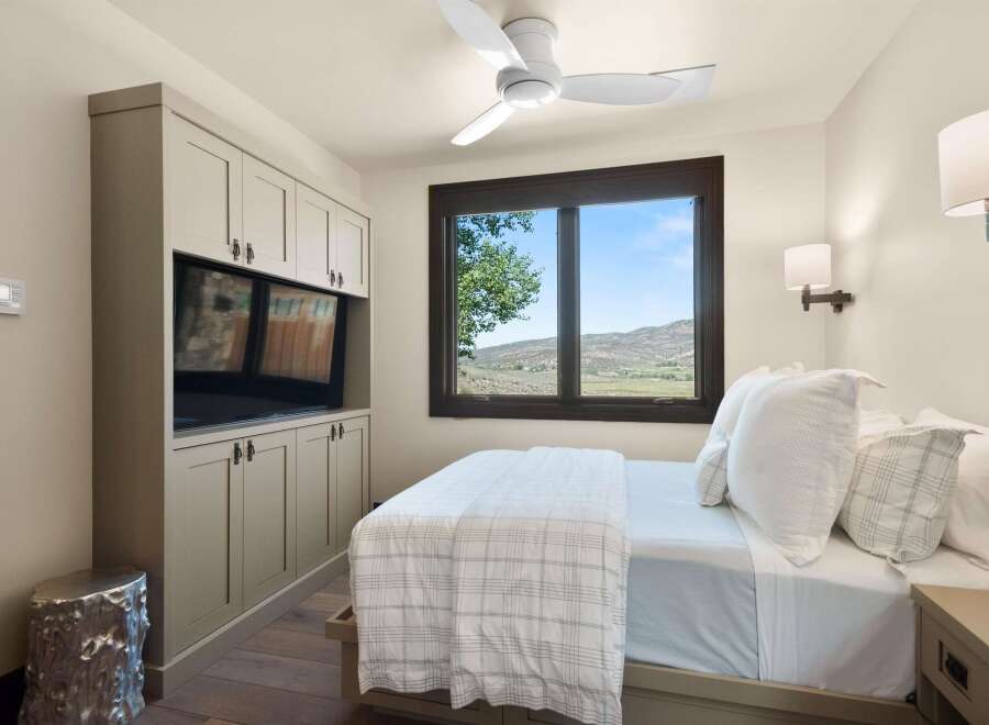 Experience serene mountain living in this charming bedroom, featuring a built-in entertainment center and a large window with breathtaking views.