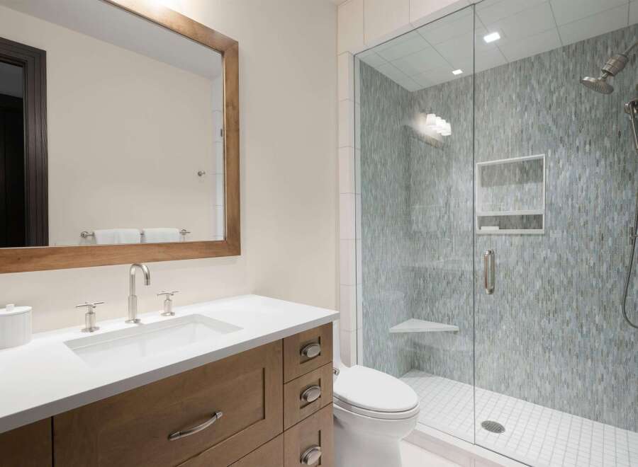Experience modern luxury in this stunning bathroom, featuring a sleek vanity with a white countertop and a spacious glass-enclosed shower adorned with intricate mosaic tile.