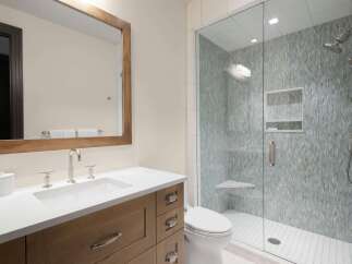 Experience modern luxury in this stunning bathroom, featuring a sleek vanity with a white countertop and a spacious glass-enclosed shower adorned with intricate mosaic tile.