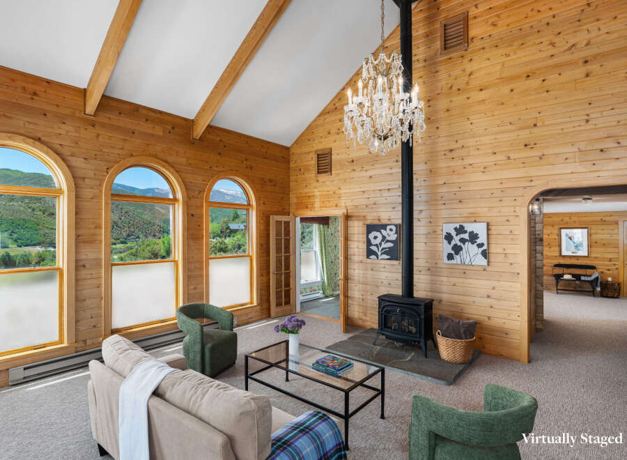 Experience breathtaking mountain views from this stunning living room, featuring a vaulted wood-paneled ceiling and a grand crystal chandelier.