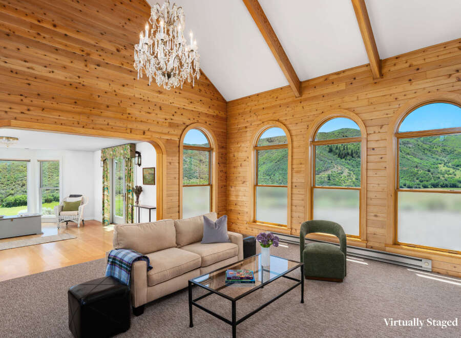 Experience breathtaking mountain views from this stunning living room, featuring a vaulted wood-paneled ceiling and a grand crystal chandelier.
