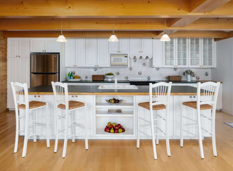 This charming kitchen features white cabinetry, a stainless steel refrigerator, and a spacious island with bar stools, perfect for casual dining.