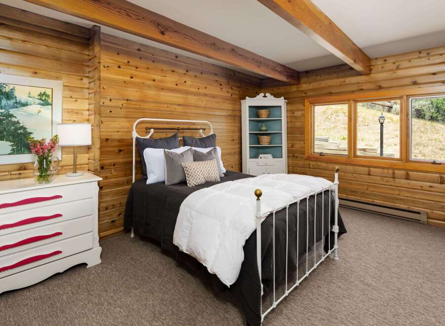 Experience rustic charm in this cozy bedroom featuring warm wood-paneled walls and exposed beams.