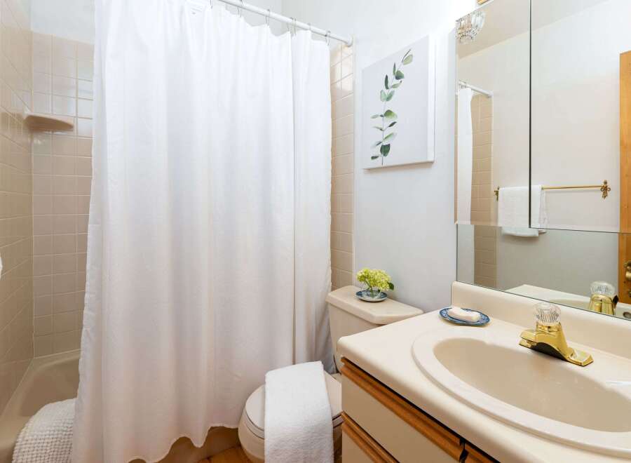This charming bathroom features a light-colored tiled shower and tub area, complemented by a crisp white shower curtain.