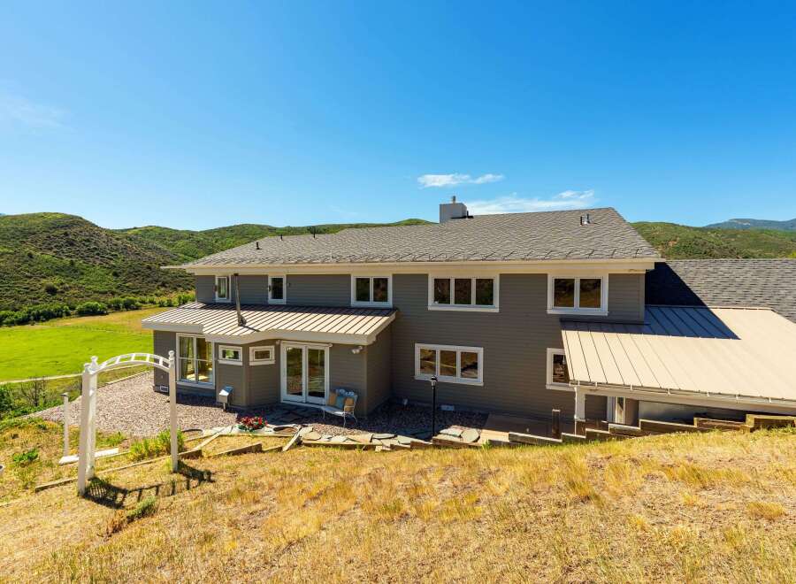 Nestled amidst rolling green hills and under a clear blue sky, this stunning property offers a serene retreat.