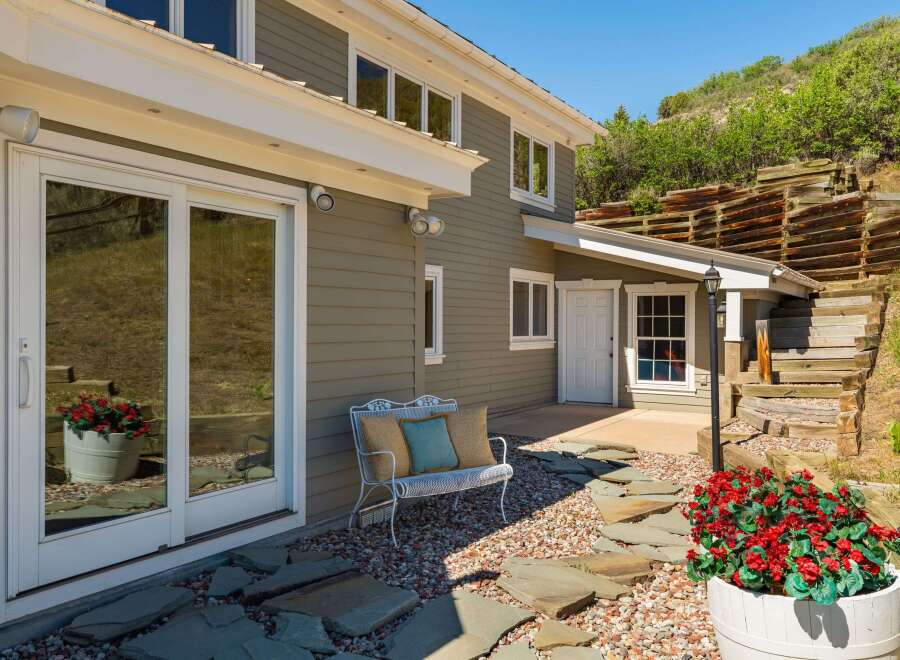 Enjoy outdoor living with this charming patio featuring a white metal bench with decorative pillows and a stone pathway leading to a lush garden.