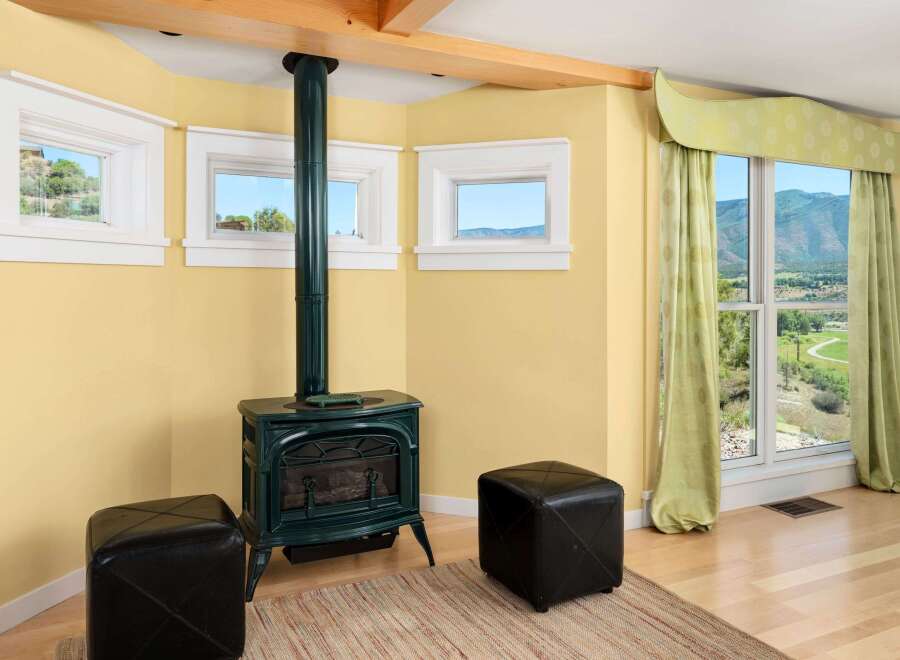 Cozy up by the green cast-iron stove in this charming room, featuring three picturesque windows offering stunning views of the surrounding landscape.