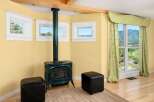 Cozy up by the green cast-iron stove in this charming room, featuring three picturesque windows offering stunning views of the surrounding landscape.