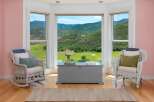 Experience breathtaking mountain views from this charming room, featuring a cozy seating area with two wicker chairs and a large bay window.