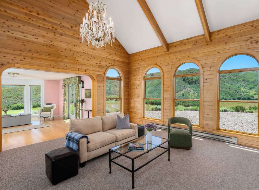 Experience breathtaking mountain views from this stunning living room, featuring a vaulted wood-paneled ceiling and a grand crystal chandelier.